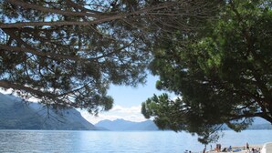 A lakeside view with a beach, mountains in the background, and people swimming and relaxing. - Casa Bel Sit by Interhome (Acquaseria)