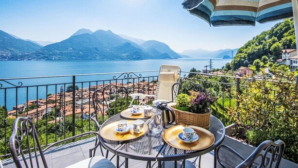 A balcony with a table set for tea, overlooking a lake and mountains. - Casa Bel Sit by Interhome (Acquaseria)