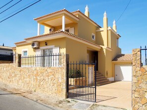 A two-story house with a stone wall, a black metal gate, and a tiled roof.