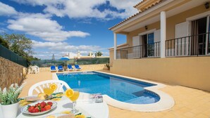 A swimming pool with sun loungers, a table with breakfast items, and a view of the surrounding landscape.