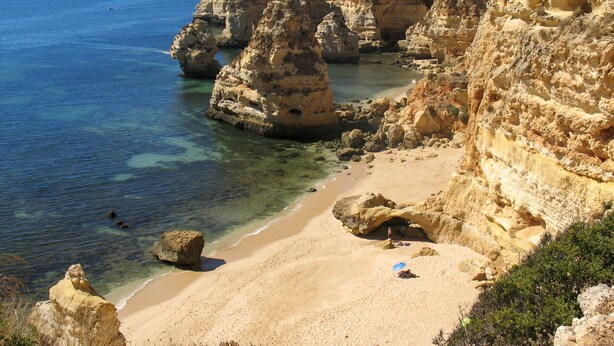 Un paisaje costero con mar azul cristalino, playa arenosa y acantilados rocosos.