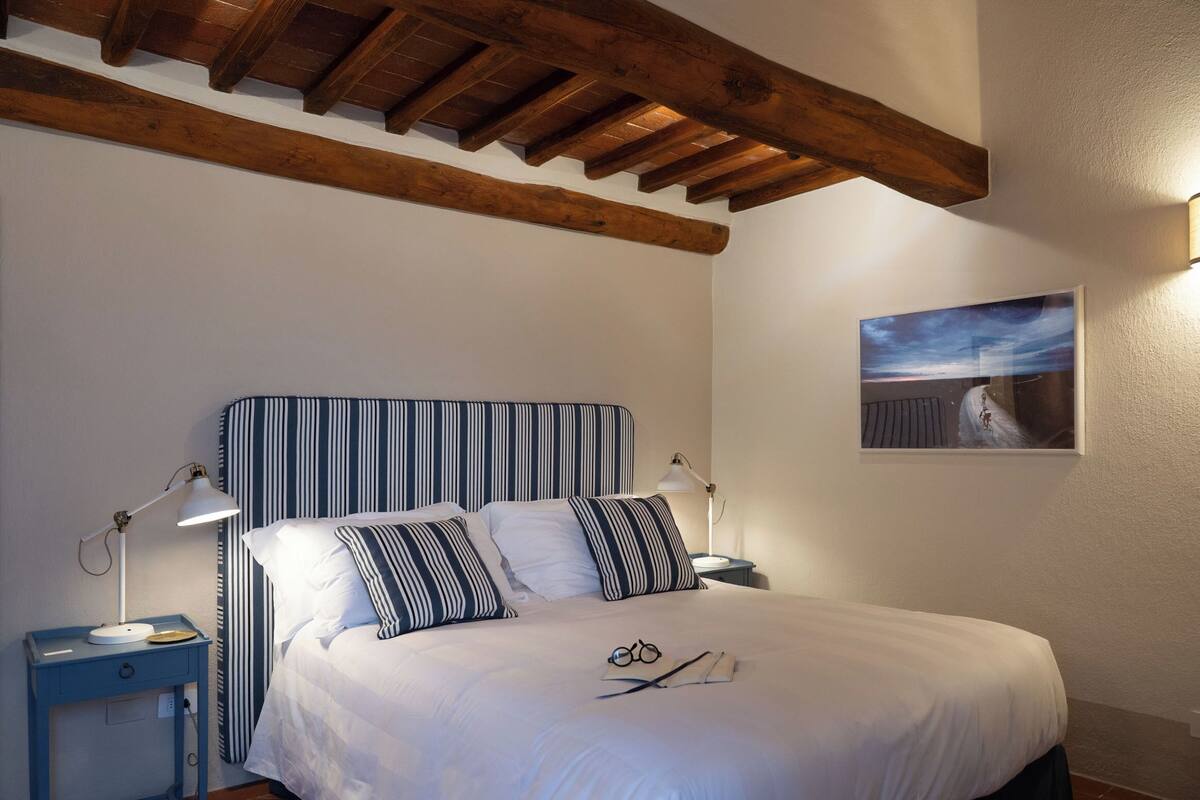 A bedroom with a striped headboard, a bed with white bedding, a nightstand with a lamp, and a painting on the wall.