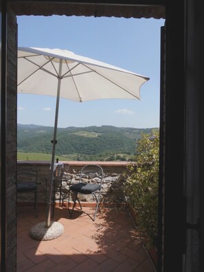 A patio with a table and chairs, an umbrella, and a view of green hills. - B&B Borgolecchi (Gaiole in Chianti)