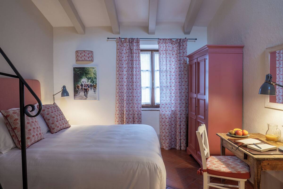 A bedroom with a bed, a desk with a chair, a wardrobe, and a window with curtains.