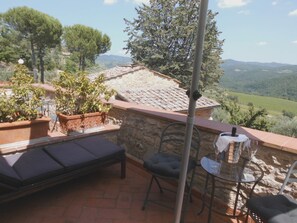 A terrace with a stone wall, a cushioned bench, a small table with a glass, and potted plants. - B&B Borgolecchi (Gaiole in Chianti)