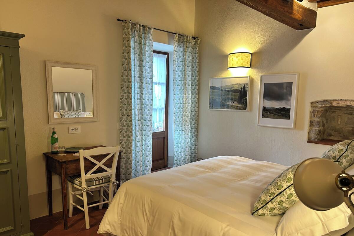 A bedroom with a bed, a desk, a chair, a mirror, and a window with curtains.