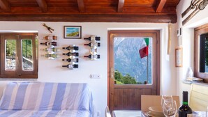 Une chambre avec un lit, une table à manger avec des verres et des bouteilles de vin, et une vue sur les montagnes par la fenêtre.