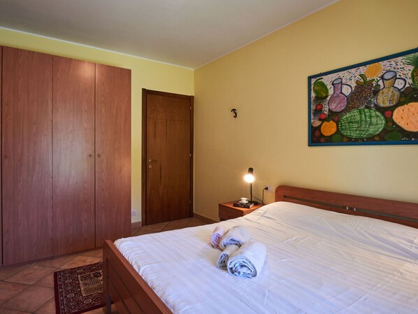 A bedroom with a bed, a nightstand, a lamp, a painting, and a wardrobe.