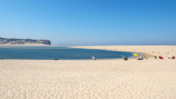 Een strand met helderblauw water, een zandstrand en een klif op de achtergrond.
