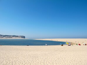 En strand med kristallklart blått vatten, en sandstrand och en klippa i bakgrunden.