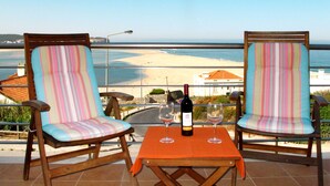 Twee gestreepte stoelen met een tafel en een fles wijn ertussen, met uitzicht op een strand.