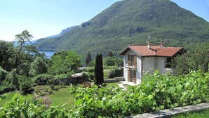 Une maison avec un toit rouge, entourée d’une végétation luxuriante et avec une montagne en arrière-plan.