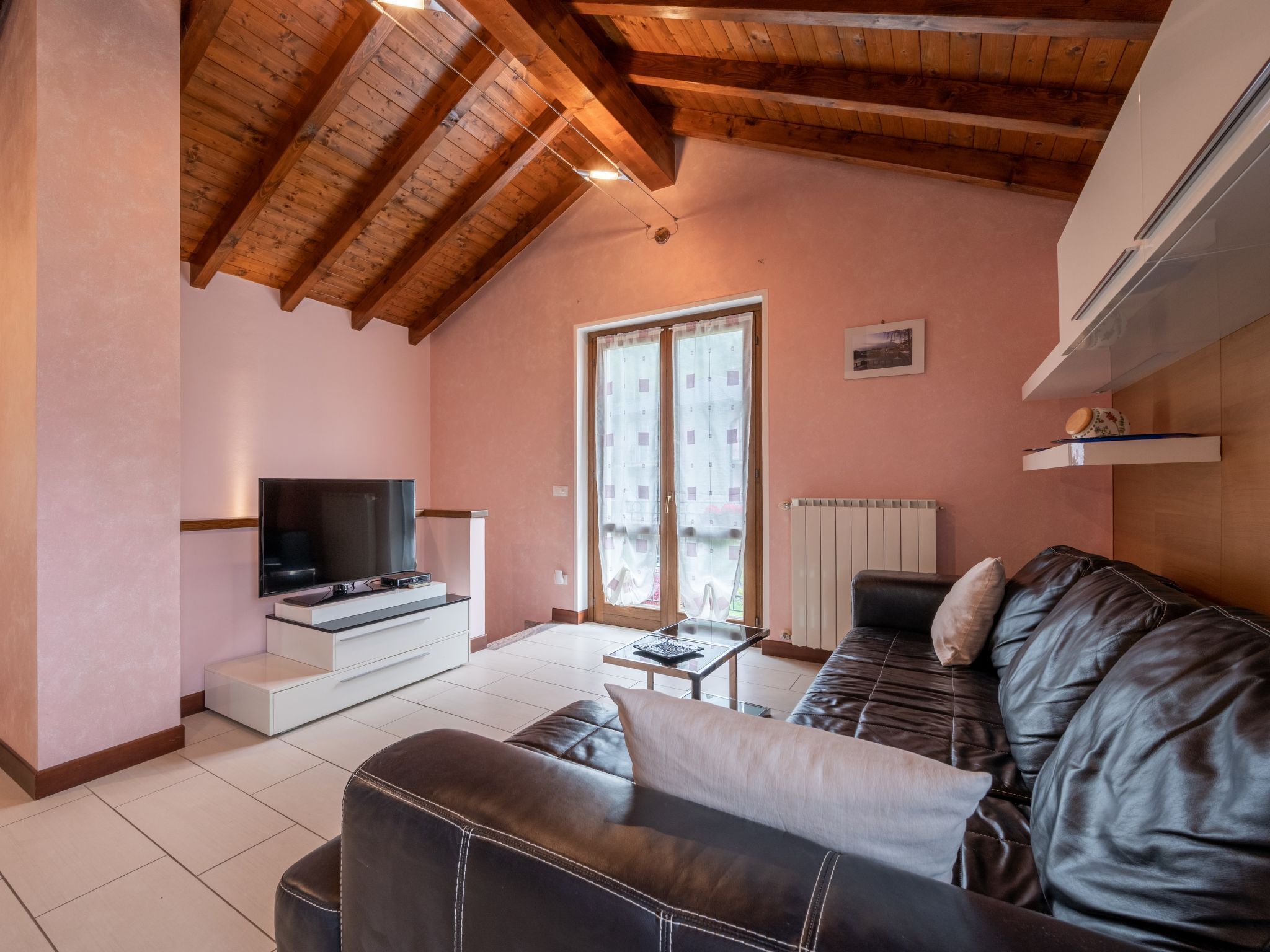 A living room with a TV, leather sofa, wooden ceiling beams, and a radiator.