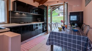 Une cuisine moderne avec des meubles noirs, un plan de travail en acier inoxydable et un coin repas agrémenté d’une nappe à carreaux.