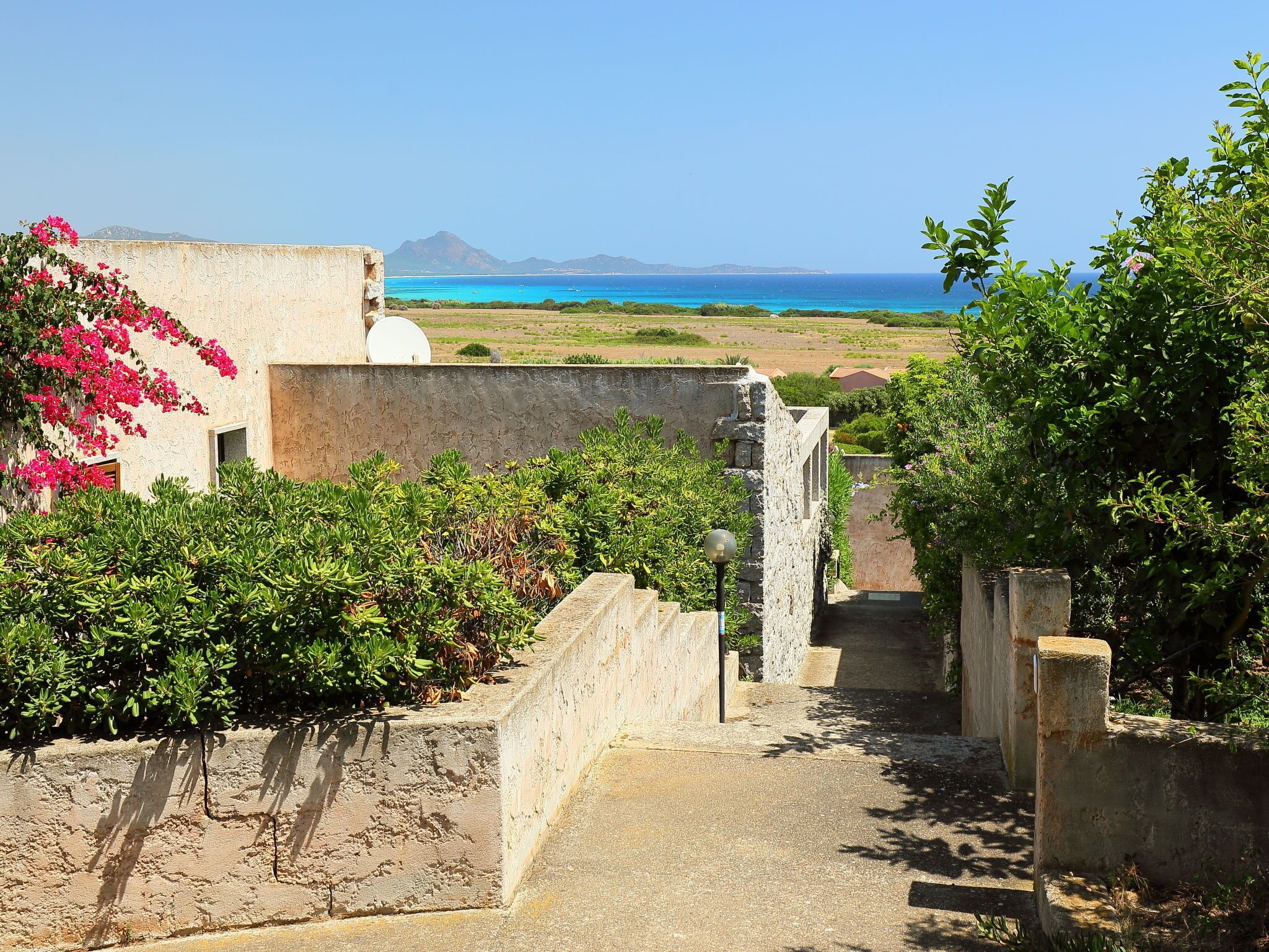 Un sentier menant à un bâtiment d’où l’on a une vue sur la mer et les montagnes.