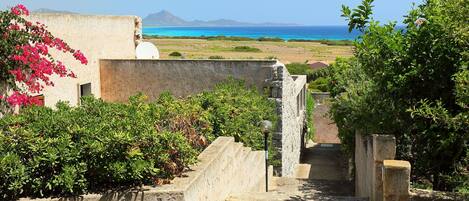 A pathway leading to a building with a view of the sea and mountains.