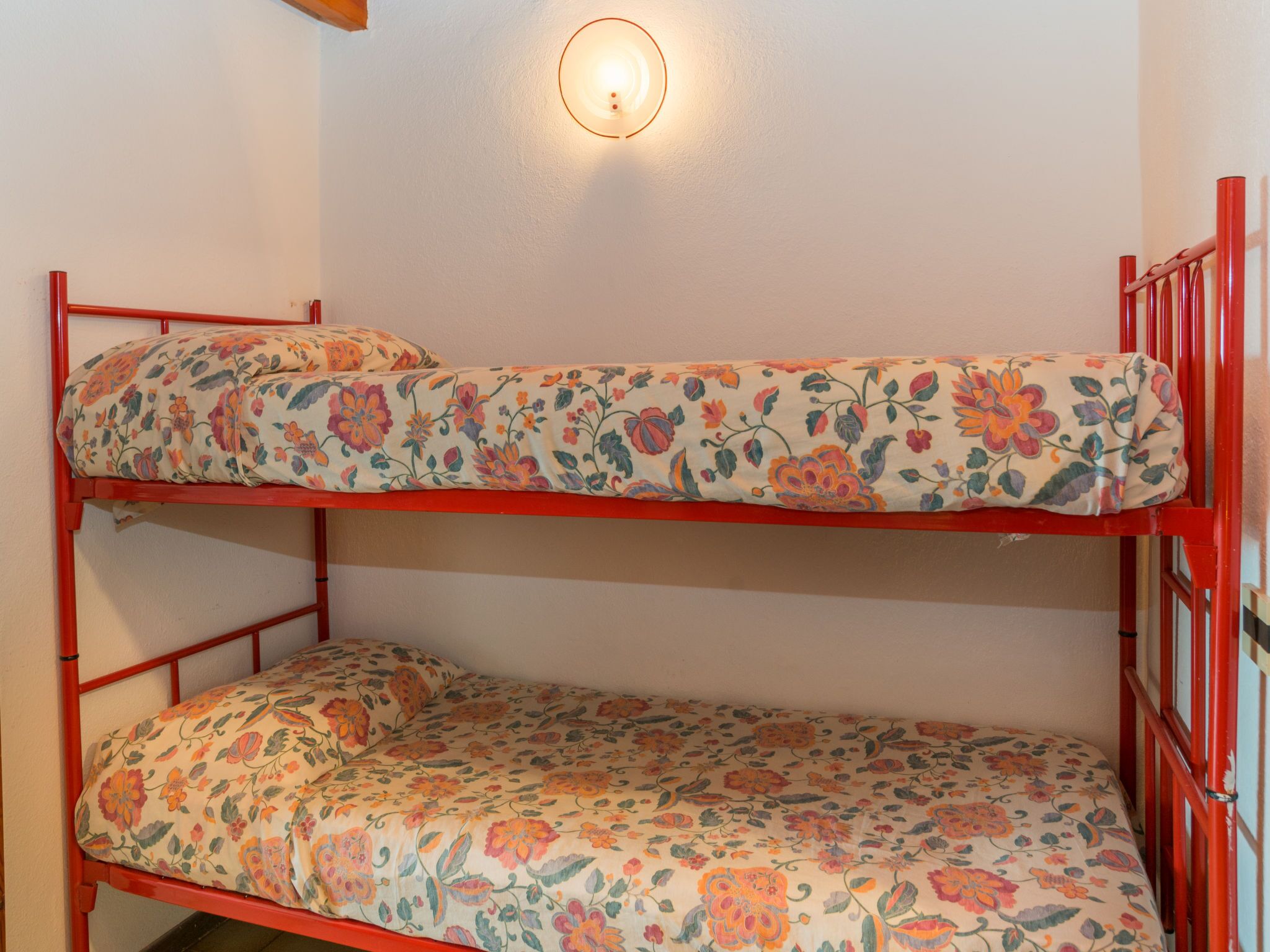 A bunk bed with floral-patterned bedding and a wall-mounted light fixture.