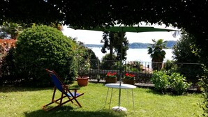 Eine Terrasse mit Liegestuhl, einem kleinen runden Tisch und Kübelpflanzen.