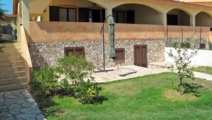Un bâtiment à deux étages doté d’une façade en pierre, de nombreuses fenêtres avec volets et d’un espace extérieur couvert agrémenté d’une pergola.