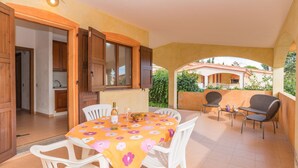 Une terrasse avec une table dressée pour deux personnes, des chaises blanches et un fauteuil en osier.