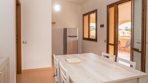 Une cuisine compacte comprenant un réfrigérateur, une table à manger avec des chaises et une porte-fenêtre coulissante donnant sur un espace extérieur.