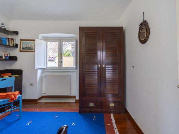 Une pièce avec une armoire en bois, un radiateur, une fenêtre donnant sur un beau paysage, une étagère remplie de livres et un tapis bleu.