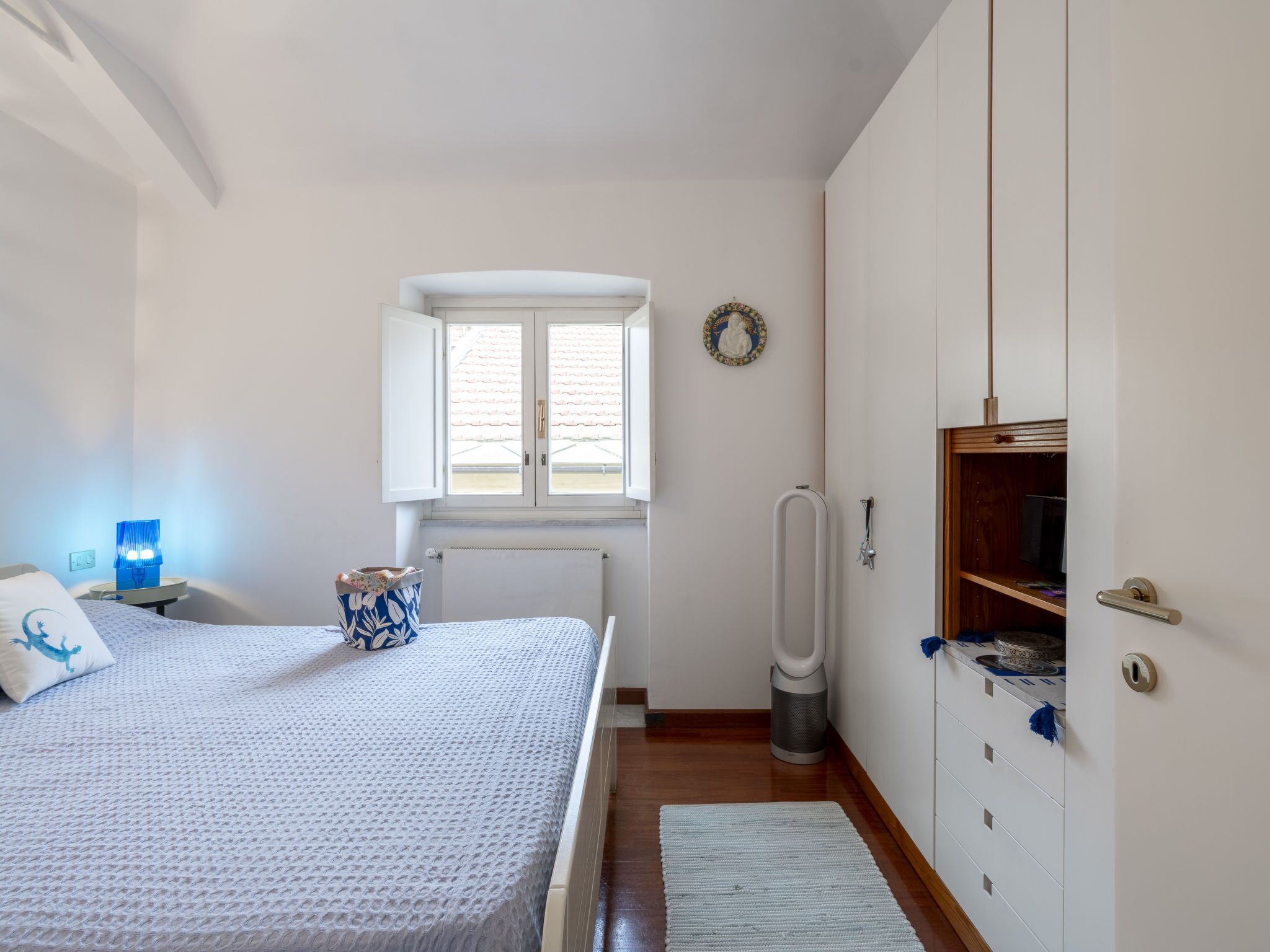 A bedroom with a bed, a nightstand, a radiator, a window, a toilet, and a wardrobe.