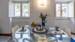 A dining area with a glass table, white chairs, and a vase with flowers.