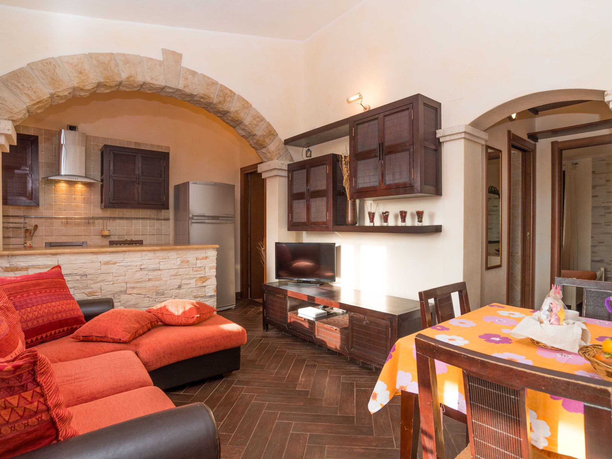 A cozy living area with a stone fireplace, dark wooden cabinets, a television, and a dining table with a floral tablecloth.
