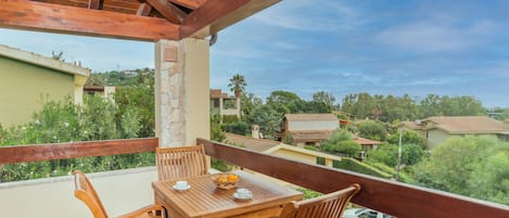 A wooden balcony with a table and chairs, overlooking a residential area with houses and greenery.