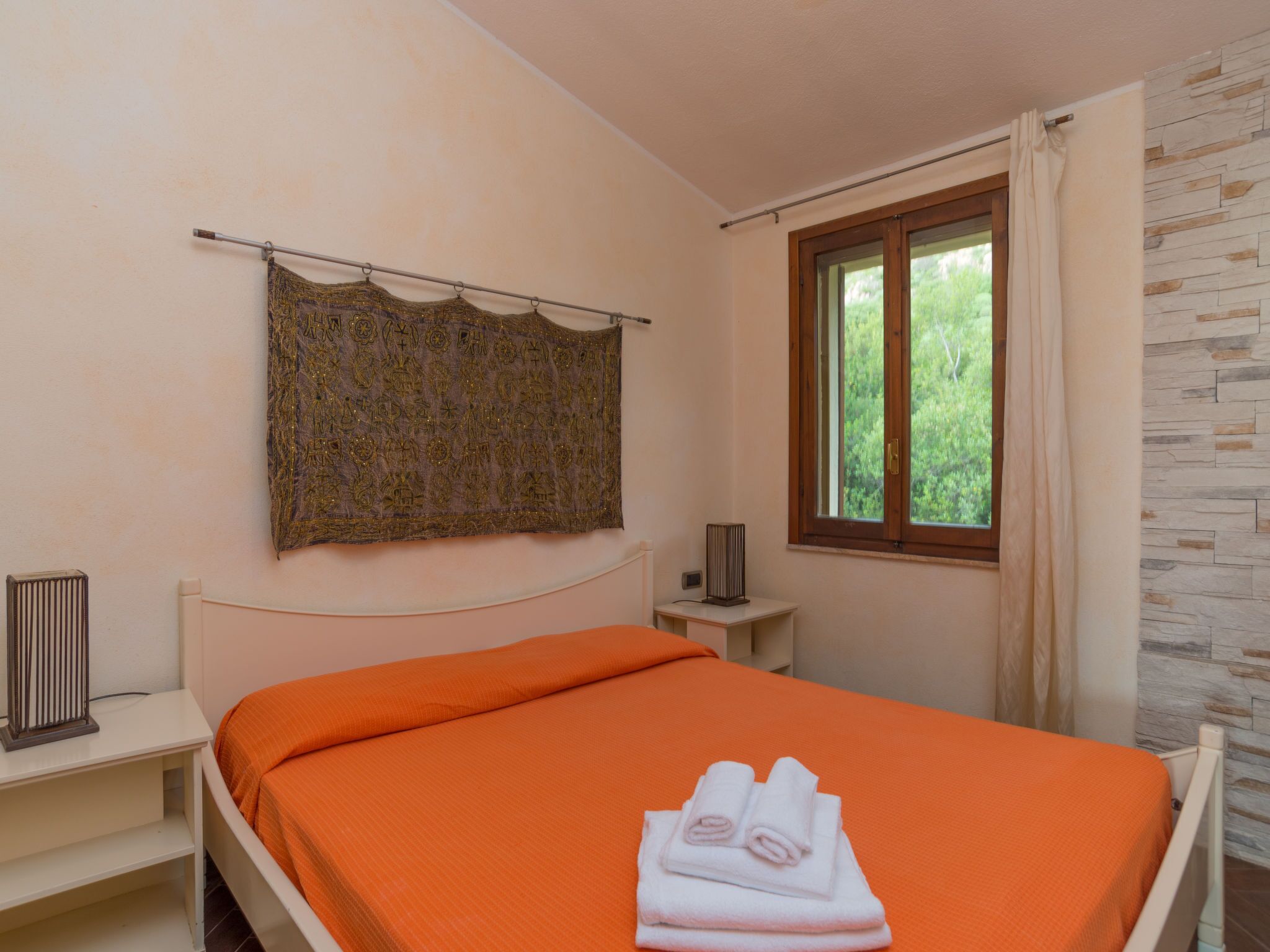 A bedroom with a bed, a radiator, a window with curtains, and a wall with a stone-like pattern.