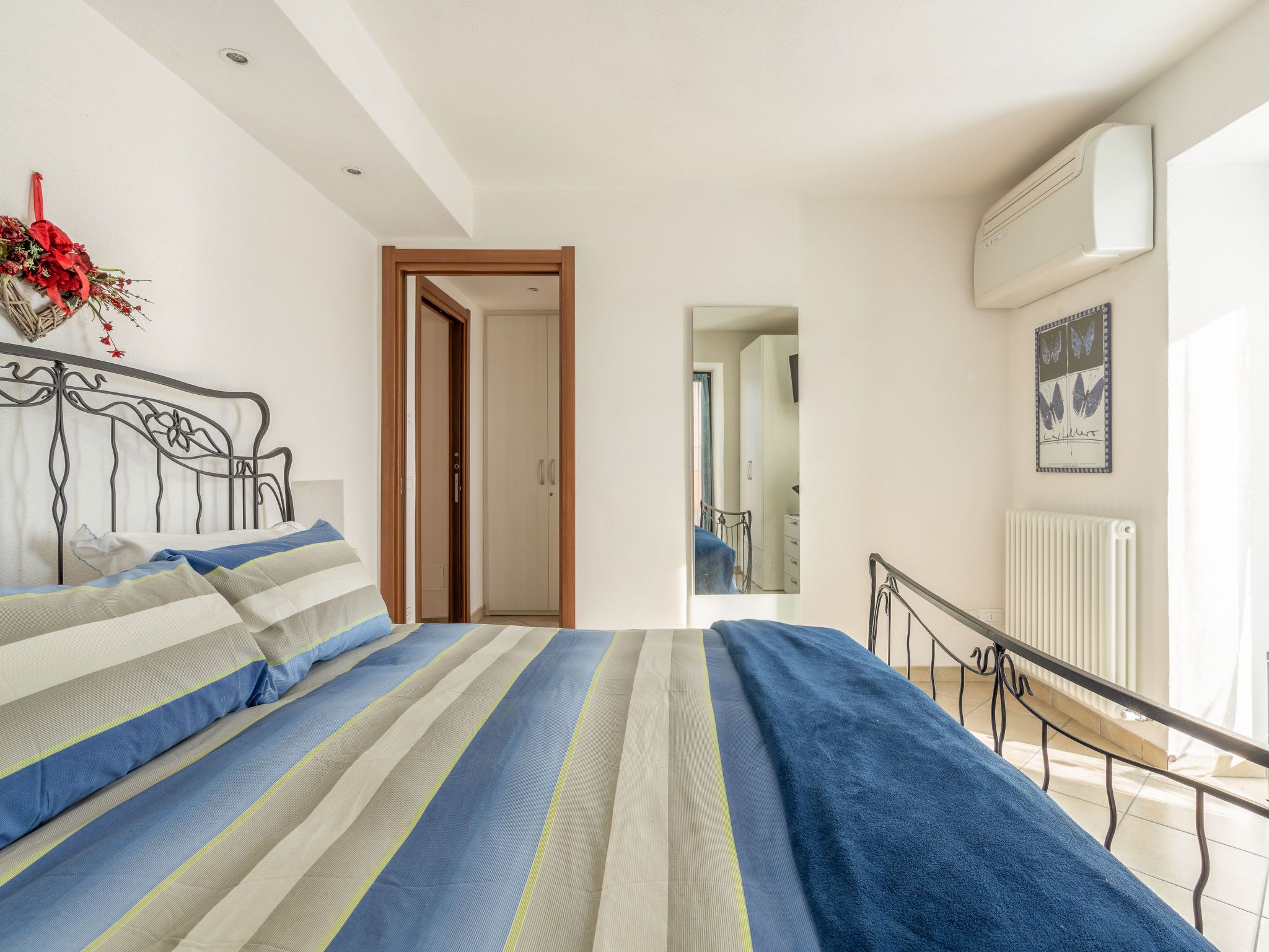 Ein Schlafzimmer mit einem Bett, einem Heizkörper, einem Fenster und einer Tür zu einem anderen Raum.