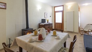 Et spiseområde med et bord dækket til fire personer, en sort komfur, et fjernsyn på et træskab og en fletstol.