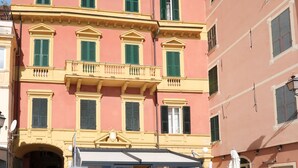 Un immeuble à plusieurs étages, doté d’une façade rose, de volets verts et d’un balcon orné de balustrades.