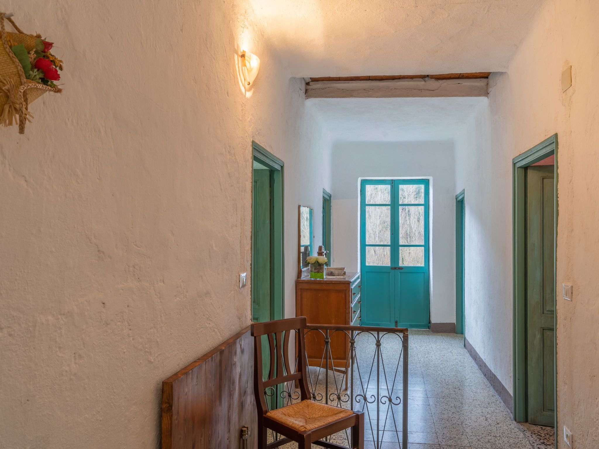 A narrow hallway with a wooden bench, a green door at the end, and a wall-mounted light fixture.