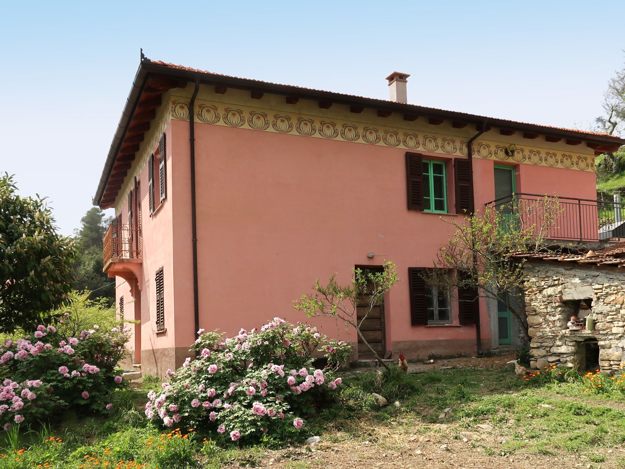 A pink building with a stone structure, a balcony, and a garden with pink flowers.