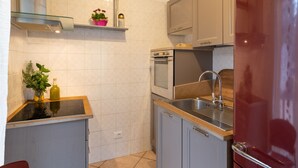 A compact kitchen with a built-in oven, a stainless steel sink, and a red refrigerator.