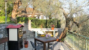An outdoor patio area with a stone table and chairs, a small barbecue grill, and a stone wall.