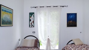 A bedroom with two beds, a window with a curtain, and artwork on the walls. - La Perla del Mediterraneo by Interhome (Cervo)
