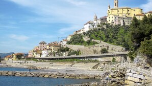 A coastal town with historic buildings, a prominent church with a bell tower, and a stone staircase leading down to the beach. - La Perla del Mediterraneo by Interhome (Cervo)