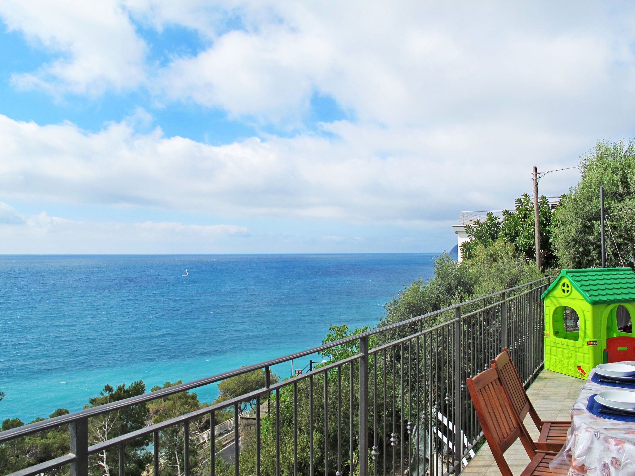 A balcony with a view of the sea, a small green playhouse, and a table with chairs.