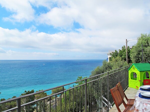 A balcony with a view of the sea, a small green playhouse, and a table with chairs.