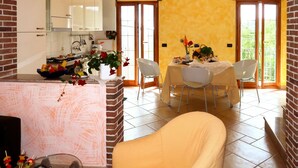 Uma sala de jantar com mesa posta para dois, cozinha ao fundo e lareira de tijolos.