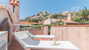 Eine Dachterrasse mit zwei weißen Lounge-Stühlen und einem Tisch, mit Blick auf eine Berglandschaft mit Häusern mit Terrakotta-Dächern.