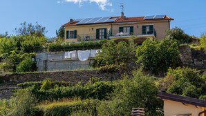 Une maison à deux étages, dotée de panneaux solaires sur le toit, avec un mur de pierre au premier plan et une végétation luxuriante tout autour.