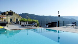 Une piscine aux eaux cristallines, agrémentée de chaises longues et d’une table, le tout entouré d’une clôture et offrant une vue sur les montagnes.