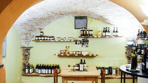 Une cave à vin avec des étagères remplies de bouteilles et de jarres, une table en bois avec des chaises, et un mur en pierre.
