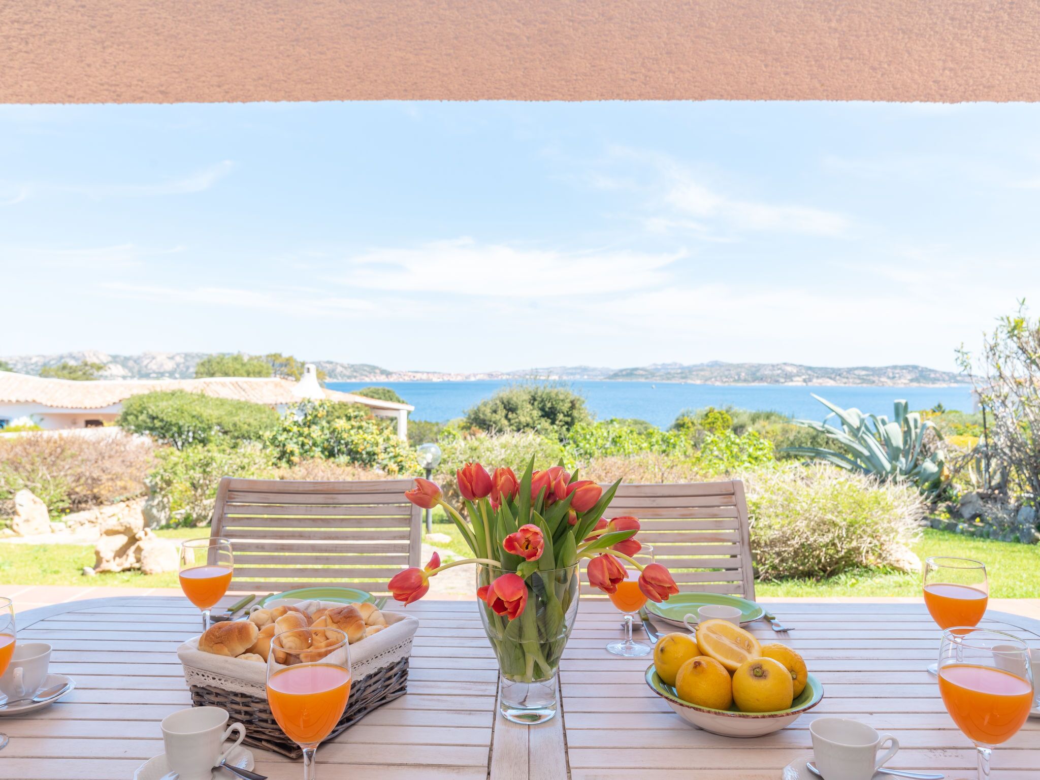 A table set with bread, lemons, and tulips, overlooking a coastal landscape.