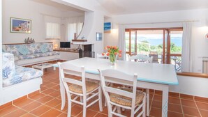A bright, well-lit room with a dining table, chairs, a sofa, a TV, and a view of the sea through a large window. - Mare Blù by Interhome (Palau)