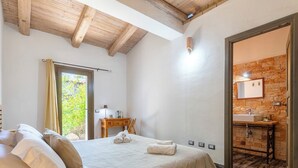 A bedroom with a bed, a desk, a window, and a bathroom with a stone wall. - Oliviola by Interhome (Valledoria)